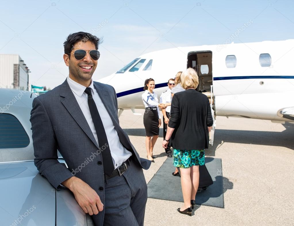 Happy Businessman Leaning On Car At Airport Terminal