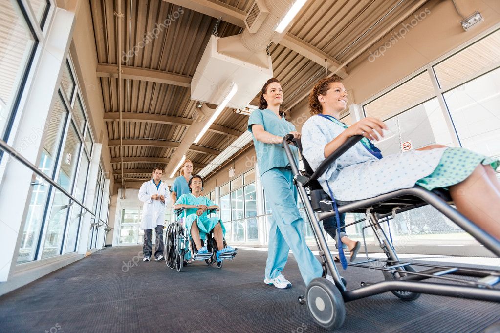 Nurses Pushing Patients On Wheelchairs With Doctor At Corridor