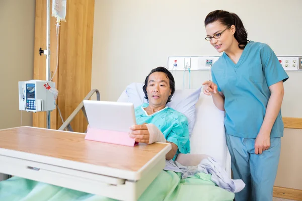 Patient nutzt digitales Tablet, während Krankenschwester darauf zeigt — Stockfoto