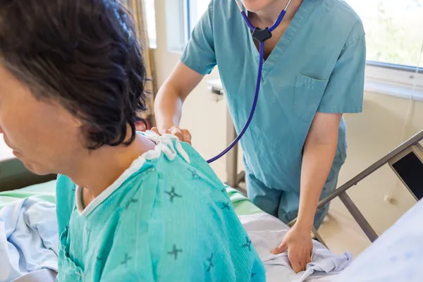 Verpleegkundige onderzoek patiënt terug met stethoscoop — Stockfoto
