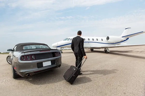 Affärsman står med bil och privata jetplan på terminal — Stockfoto