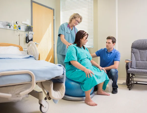 Enfermeira e homem assistindo a mulher grávida em bola de exercício — Fotografia de Stock