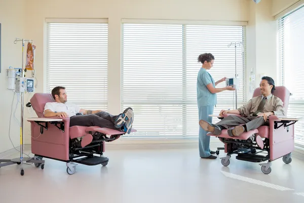 Infermiera regolazione IV macchina mentre i pazienti sdraiati sulla sedia — Foto Stock