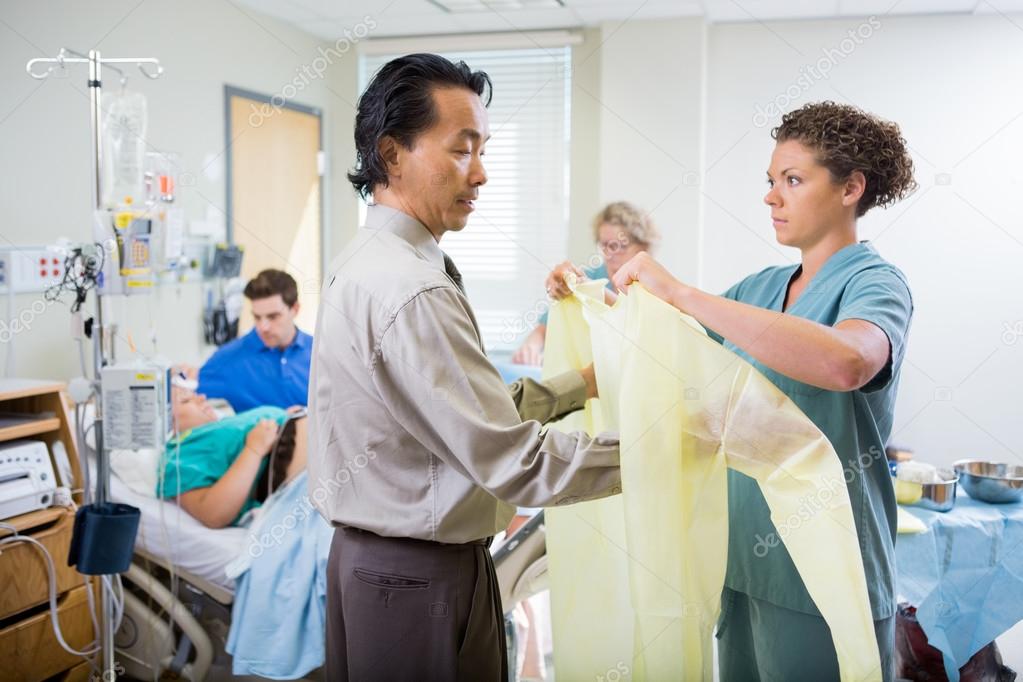 Nurse Assisting Doctor In Wearing Operation Gown At Hospital