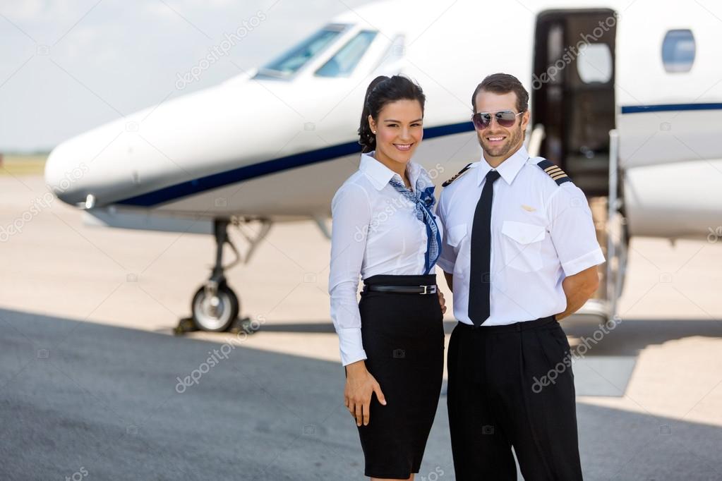 Happy Airhostess And Pilot Standing Against Private Jet