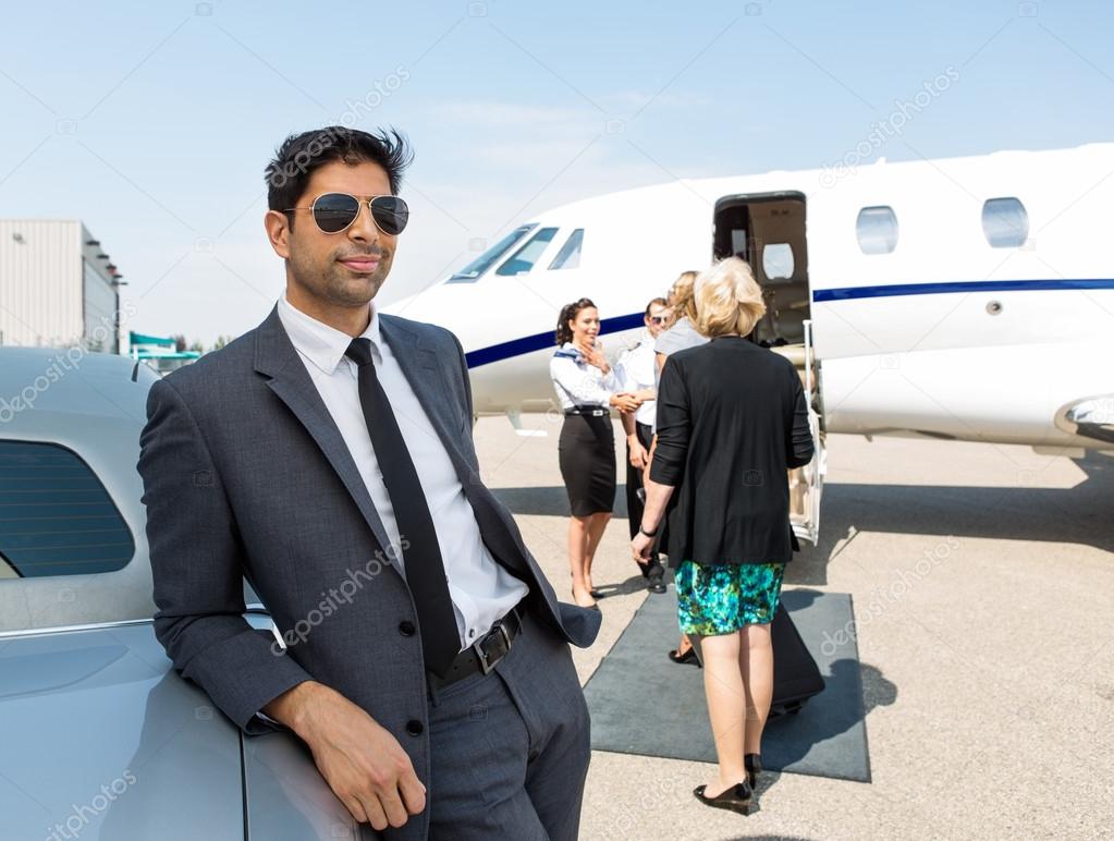 Businessman Leaning On Car At Airport Terminal