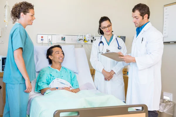 Médicos discutiendo notas mientras la enfermera y el paciente los miran — Foto de Stock