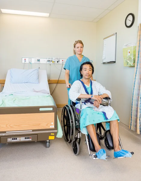 Paciente masculino sentado en silla de ruedas mientras la enfermera lo asiste — Foto de Stock