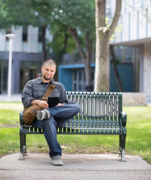 Manlig student med digital tablet på bänken på campus — Stockfoto