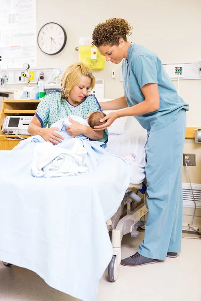 Krankenschwester hilft Frau beim Halten von Neugeborenem im Krankenhaus — Stockfoto