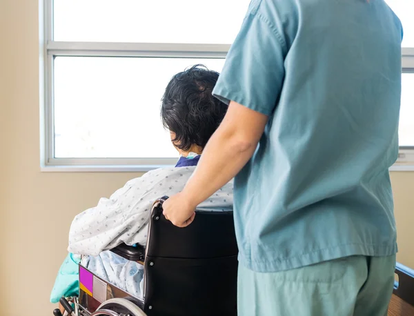Pacjent siedzi w wózku podczas pielęgniarka pomoc mu w windo — Zdjęcie stockowe
