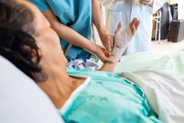 Infermiera mettendo fasciatura sulla mano del paziente mentre in piedi dal medico — Foto Stock