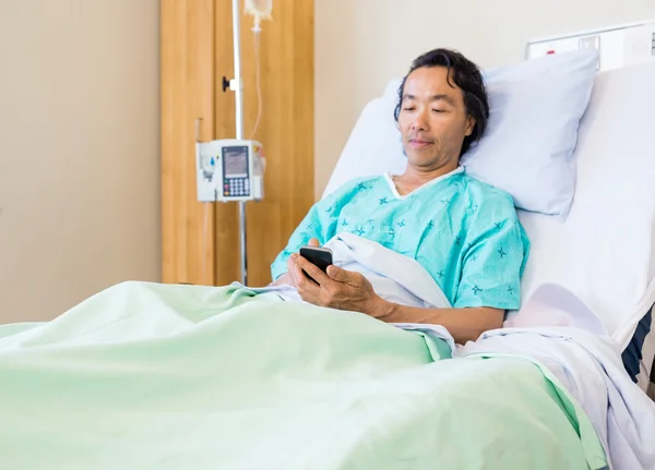 Пациент с помощью мобильного телефона на больничной койке — стоковое фото