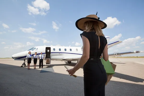 Mujer caminando hacia piloto y azafatas contra jet privado — Foto de Stock