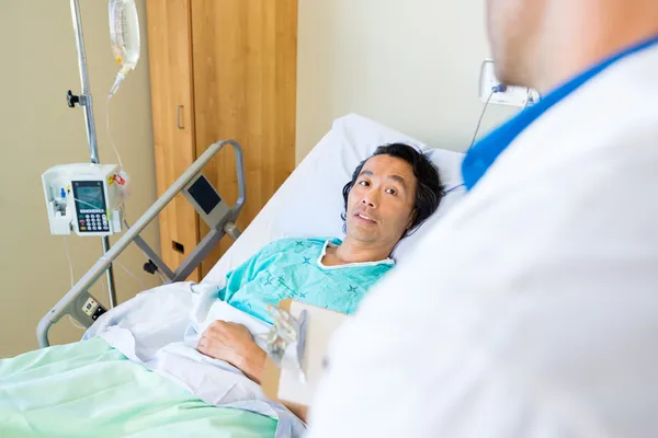 Paciente olhando para o médico enquanto deitado na cama no hospital — Fotografia de Stock