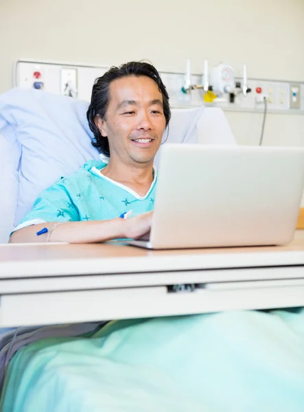 Paciente feliz usando el ordenador portátil en la cama del hospital —  Fotos de Stock