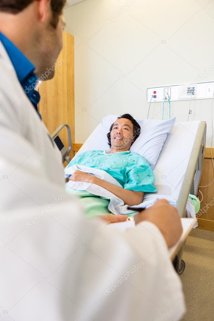 Patient Looking At Doctor Writing On Clipboard On Hospital Bed