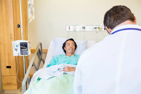 Maschio paziente guardando medico mentre sdraiato sul letto d'ospedale — Foto Stock