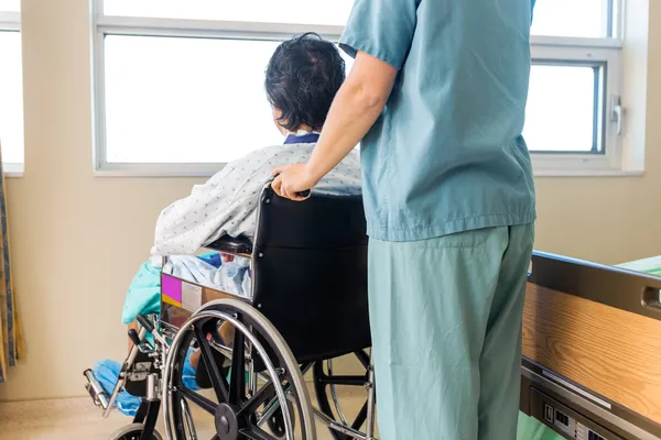 Infirmière tenant la poignée du fauteuil roulant du patient par fenêtre — Photo