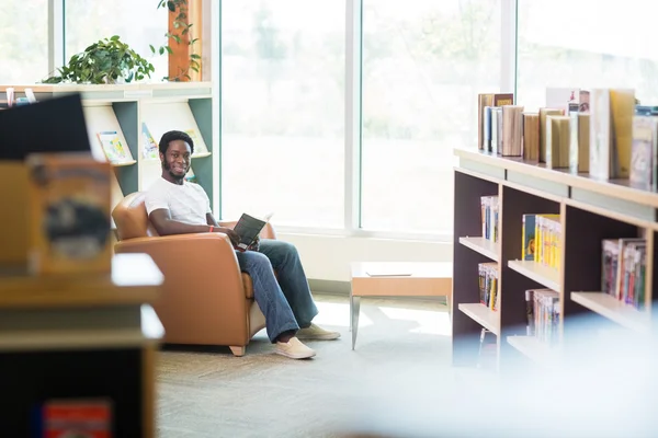 Lächelnder Student liest Buch in Bibliothek — Stockfoto