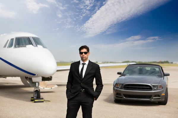 Empreendedor em pé na frente do carro e jato privado — Fotografia de Stock