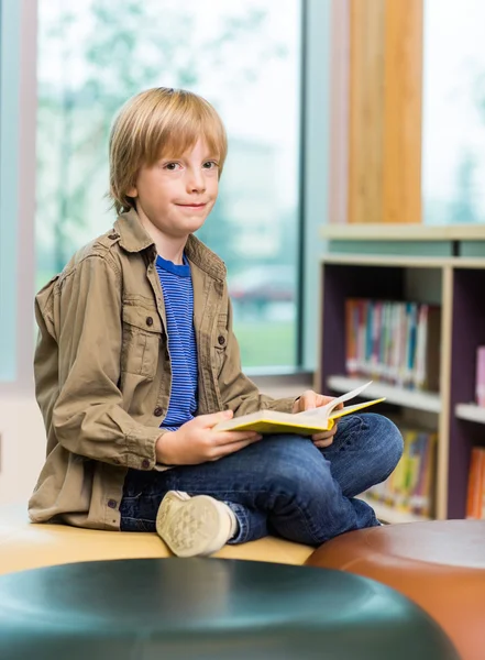 Lycklig pojke läser bok i biblioteket — Stockfoto