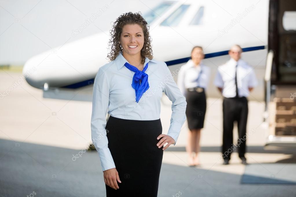 Airhostess With Hand On Hip Standing At Airport Terminal