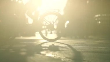 Bisikletlerin silueti gün batımına karşı caddeyi geçiyor. Şehir hayatı, trafik ve seyahat kavramı 