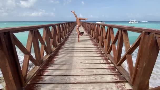 Circo feminino flexível fazendo suporte no cais com fundo do mar e do céu. Viagens, férias e conceito de estilo de vida saudável — Vídeo de Stock