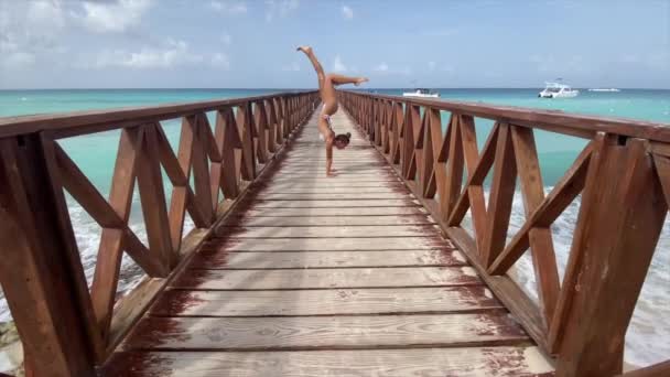 Circo femenino flexible haciendo soporte de manos en el muelle con cielo y fondo marino. Individualidad, excepcional y originalidad. — Vídeos de Stock