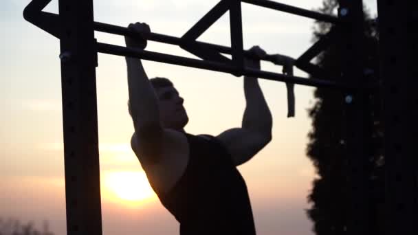 Homem musculoso a fazer pullups no fundo do céu do pôr do sol. Conceito de força de vontade, motivação e paixão — Vídeo de Stock