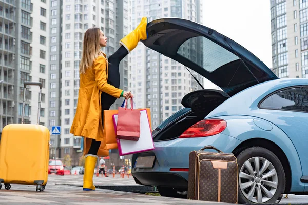 Mujer flexible sosteniendo split y sacando bolsas del coche. Concepto de individualidad, creatividad y confianza en sí mismo — Foto de Stock