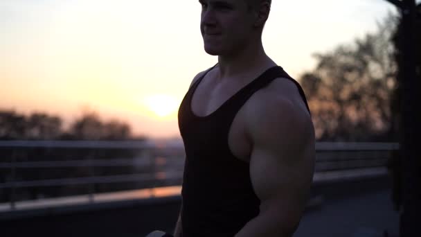 Белый белый мускулистый мужчина поднимает гантели на фоне заката. Концепция желания, воли и потенциала — стоковое видео