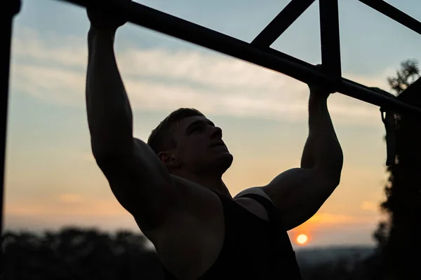 日没の空の背景でプルアップを行う筋肉の男。石灰岩,健康的なライフスタイルとワークアウトの概念 — ストック写真