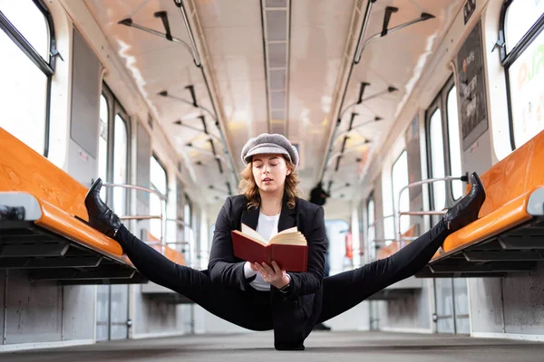 Chica flexible sentado en la división en el metro y la lectura de libro. Concepto de creatividad, individualidad y confianza en sí mismo — Foto de Stock