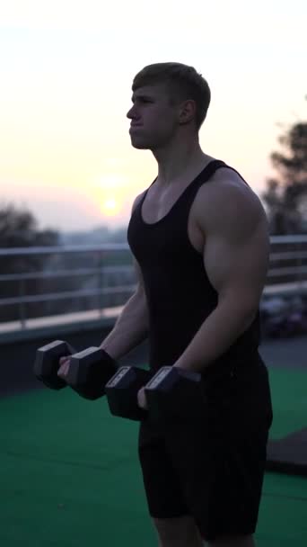 Homem musculoso branco caucasiano levantando halteres contra o fundo do céu por do sol. Conceito de força de vontade, motivação e paixão. 4k tiro vertical — Vídeo de Stock