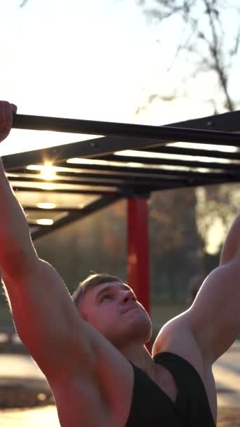 日没の空の背景でプルアップを行う筋肉の男。体操、健康的なライフスタイルとワークアウトの概念。縦の映像 — ストック動画