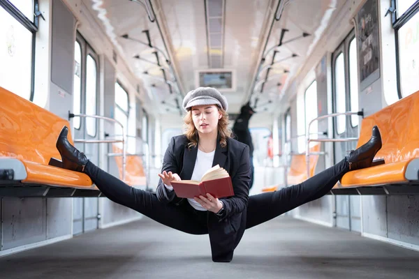 Mujer muy flexible con libro de lectura de máscaras en el vagón del metro sentado en la división gimnástica. Concepto de estilo de vida saludable y educación — Foto de Stock