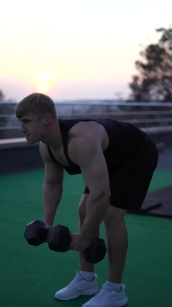 Uomo muscoloso bianco caucasico che solleva manubri sullo sfondo del cielo al tramonto. Concetto di forza di volontà, motivazione e passione. 4k colpo verticale — Video Stock