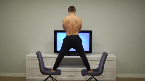 Flexibilní muž udržuje rovnováhu mezi dvěma židlemi, které se dívají na televizi. Koncept originality, kreativity a výjimečnosti — Stock video