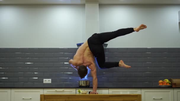 Seorang pria menjaga keseimbangan di satu sisi dan memasak makanan di dapur. Hidup sehat, konsep yoga dan kebugaran — Stok Video