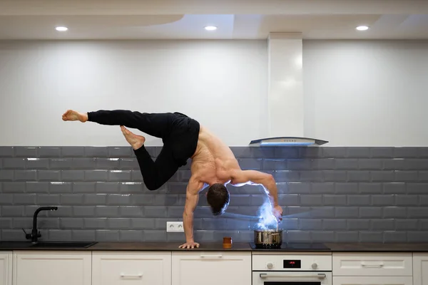 Man keeps balance on one hand and cooks food in the kitchen. Healthy lifestyle, yoga and wellness concept