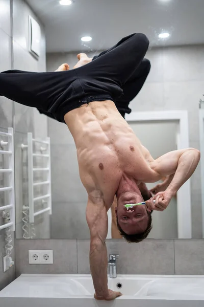 男人在浴室里倒着刷牙，一方面保持平衡。健康的生活方式、健康和瑜伽概念 — 图库照片
