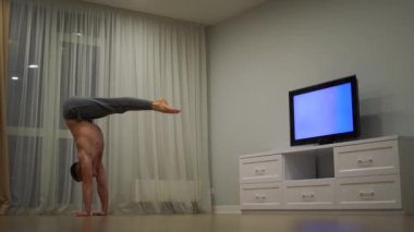 Bir adam amuda kalkıp, televizyon izleyerek dengesini koruyor. Özgünlük, yaratıcılık ve olağanüstü kavramı