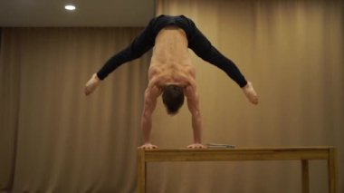 Kaslı bir adam bir elinde dengesini korur ve dizüstü bilgisayar kullanır. Sağlıklı yaşam tarzı, yoga ve amuda kalkma kavramı
