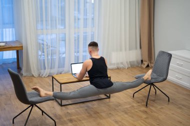 Esnek adam dizüstü bilgisayarda çalışıyor ve evde bacak ayırıyor. Yoga, sağlıklı yaşam tarzı ve sağlık konsepti
