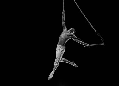 Kaslı erkek hava sirki sanatçısı dans trapeziyle performans sergiliyor.