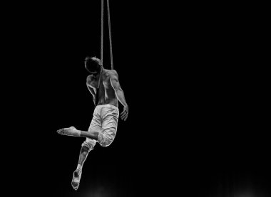 Kaslı erkek hava sirki sanatçısı dans trapeziyle performans sergiliyor.