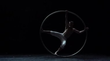 Muscular circus artist perform Cyr Wheel on a black background. Concept of desire, will and potential.