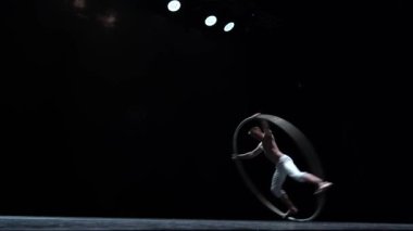 Muscular circus artist perform Cyr Wheel on a black background stage. Concept of balance, control and ability.